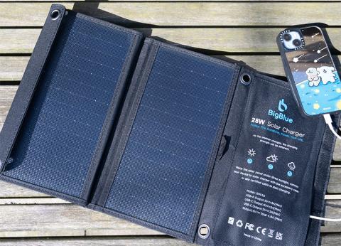 Portable solar charger, open to the sun on a park bench, with cell phone attached
