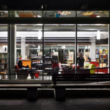 Photograph of the City Library building at night. There are people in the windows reading books and relaxing.
