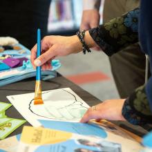 A person is holding a paintbrush and painting on a reusable mat