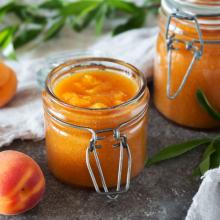 A photo of jars of peach jam with peaches in the background
