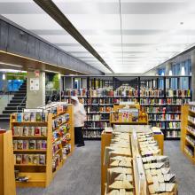 Picture of stacks of library books inside a library with one person wearing a white sweatshirt browsing