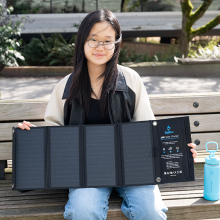 A young woman sitting on a bench holding a portable solar panel