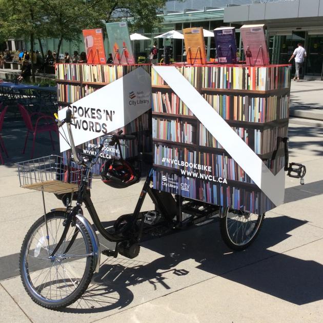 A tricycle with a large unit on the back that is open and full of books