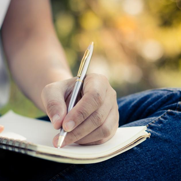 Writing for begineers Hand holding pen, writing in notebook in park