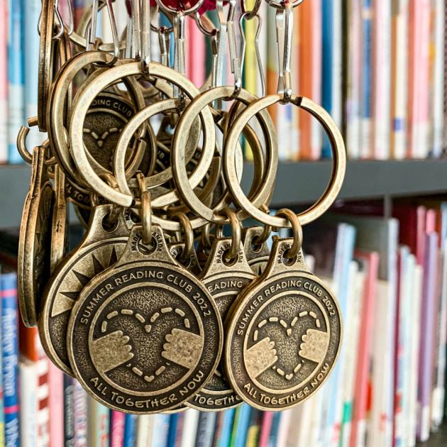 Photo of brass medals for the 2022 BC Summer Reading Club. The medals are inscribed with "All Together Now"