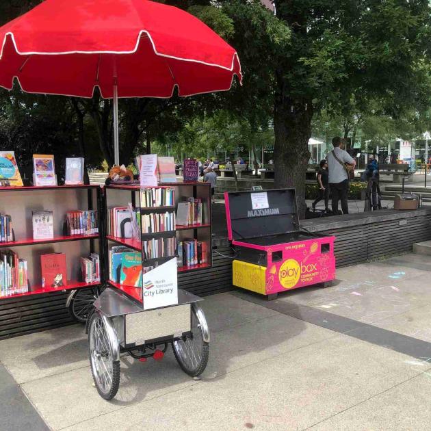 Book Bike at Lunchtime Live A cargo bike with an open cabinet in the back holds a collection of library materials in North Vancouver's Civic Plaza