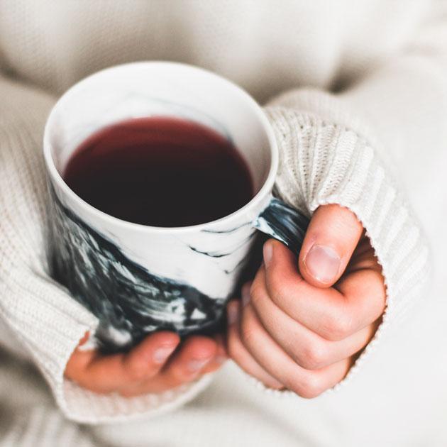 Detail photograph of two hands holding a mug of tea