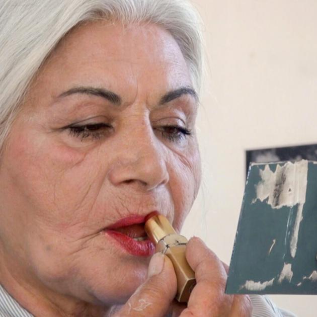 Older woman putting on bright lipstick looking at hand-held mirror