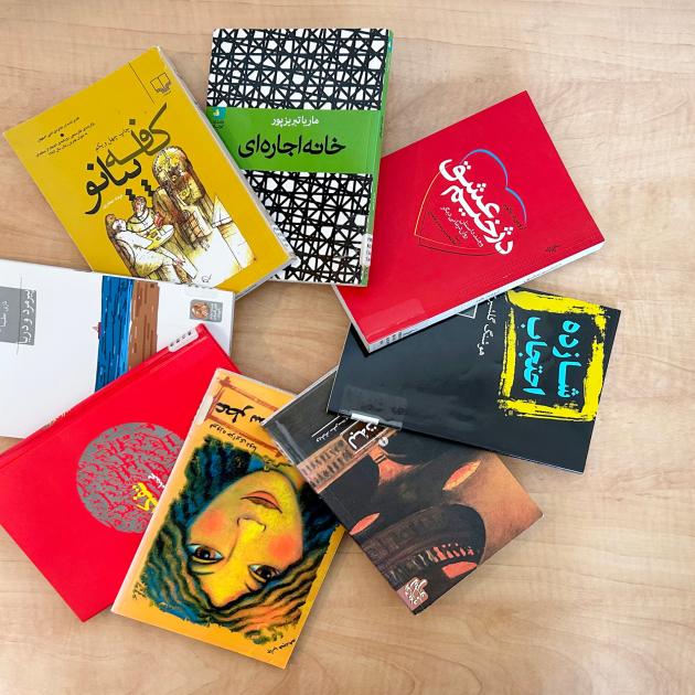 Circle of colourful Persian book covers against a wood desk