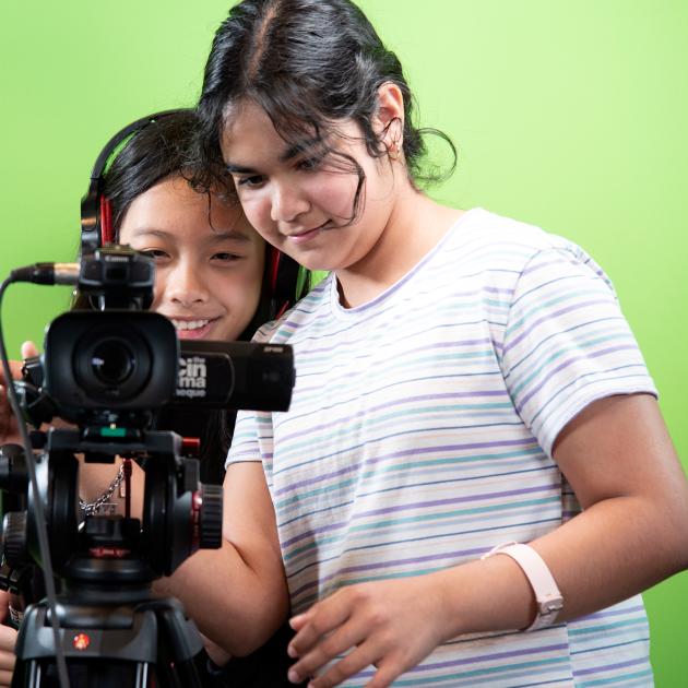 Two teens using movie camera against a green screen backdrop