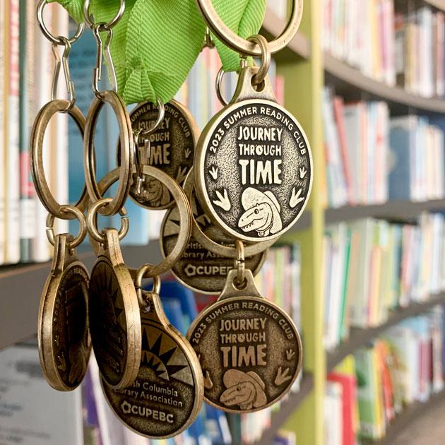 Photo of the 2023 BC Summer Reading Club medals with a row of books in the background