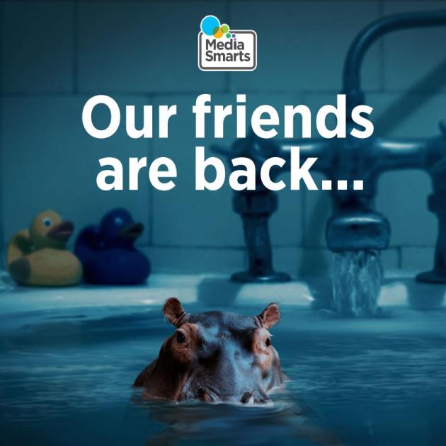 A bathtub full of water, you can see the faucet and back corner of the tub. There are two rubber duckies on the ledge - on yellow and one blue. Coming out of the water is a Hippo. At the top center is Media Smarts logo, and beneath that it says "Our friends are back..."