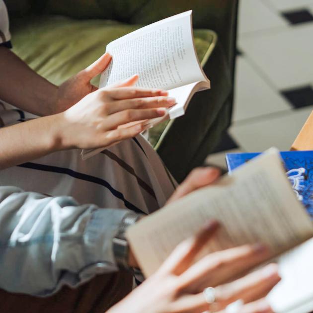 Adult English language learning book club Hands holding open books in living room scene