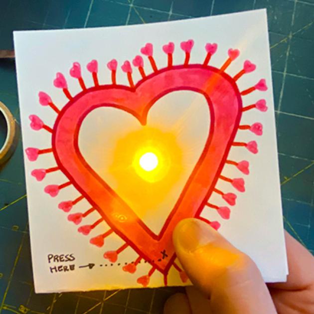 Hand-made Valentine's Day card with red heart and finger pressing button that lights up a small light in the centre