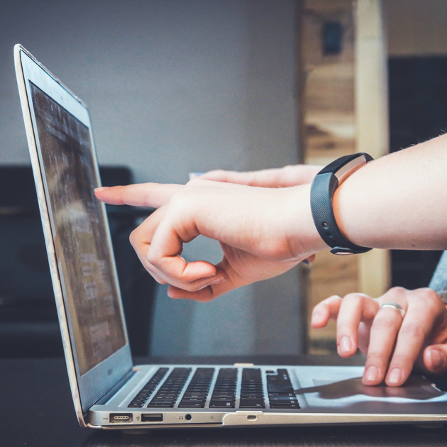 Hands pointing to and typing on a laptop.