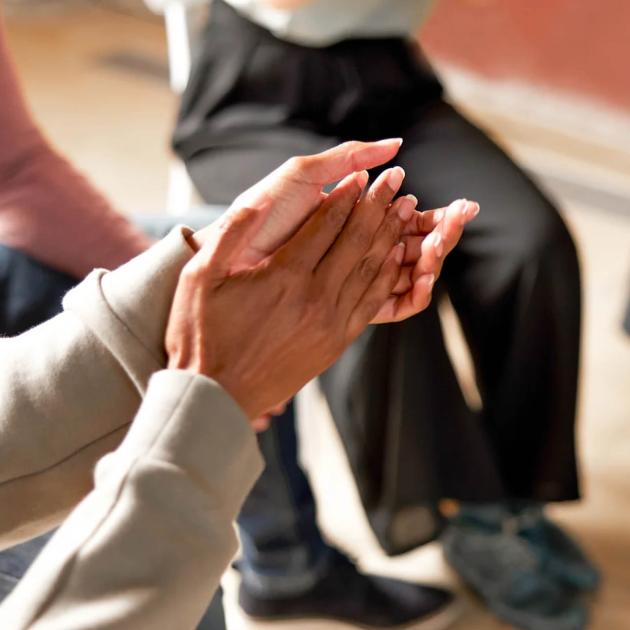 One person's hands together in support group with other people sitting in circle in background