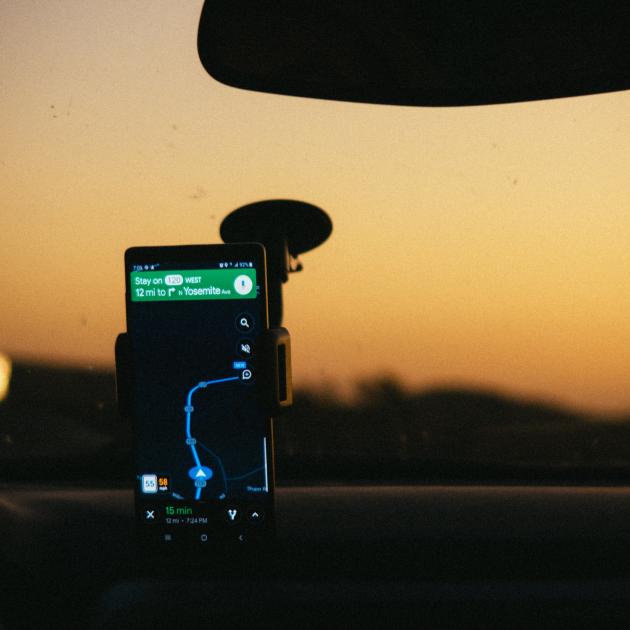 Mobile phone is in a dashboard holder and displaying a map navigation. Through the dash we can see the sky is orange.