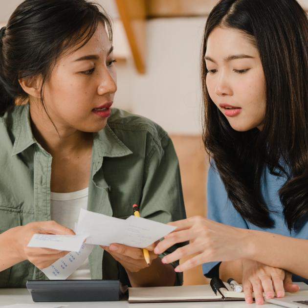 Tax for newcomers Two women discussing paperwork and accounts, holding receipts with calculator on table