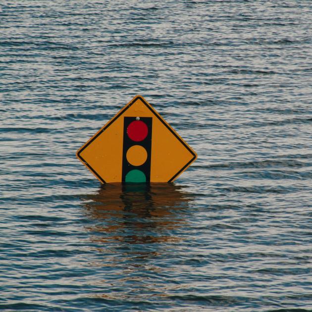 A yellow street sign signaling a traffic light is partly submerged in water