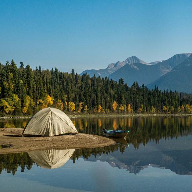 A tent near the shore of a lake, with green trees and mountains in the background