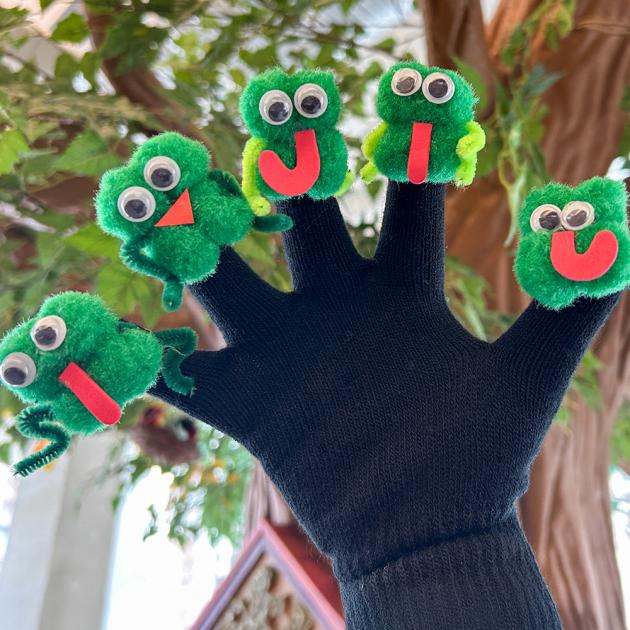 Finger play puppet workshop Hand in black glove with green frog characters at the end of each finger