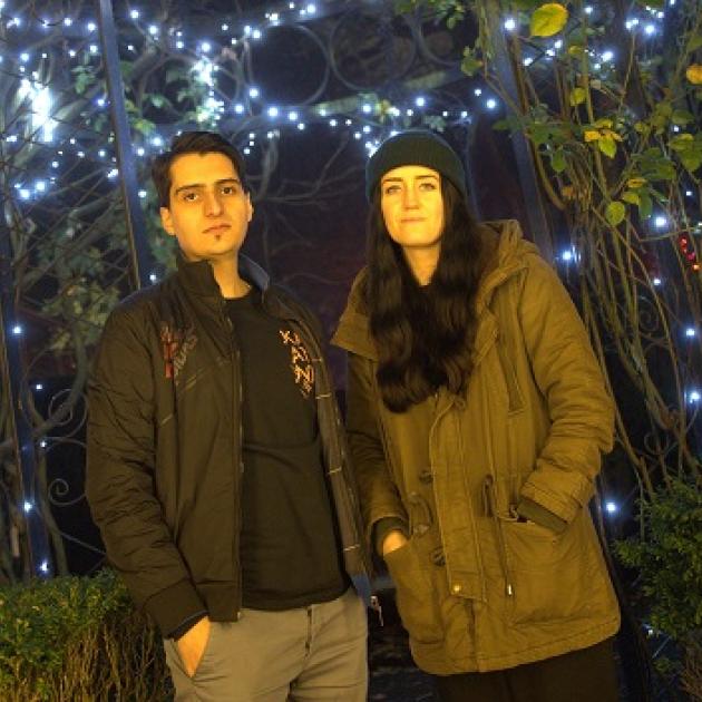 Lamin A man and a woman standing together with twinkling lights behind them.