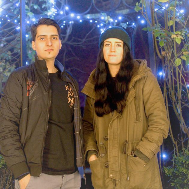 Two people standing in a garden with lights in background