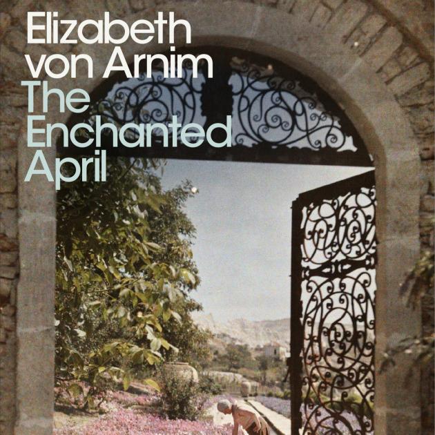 A decorative wire gate underneath a stone archway is open and leads to a courtyard where a woman is gardening