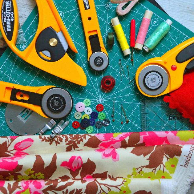 Sewing cutting tools, fabric, thread, pin cushion and buttons are splayed across a green cutting mat.