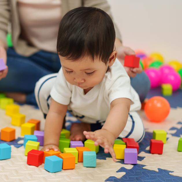 Family drop-in on Mondays Child playing on floor with brightly coloured blocks with guardian in background