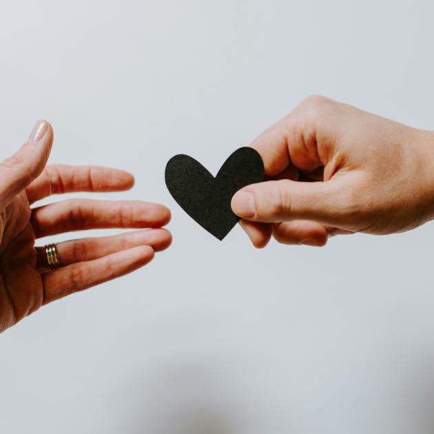 a close up of one hand giving a small black heart to another