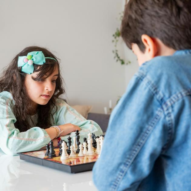 A boy and girl playing chess. Girl is wearing a blue bow in her hair A boy and girl playing chess. Girl is wearing a blue bow in her hair