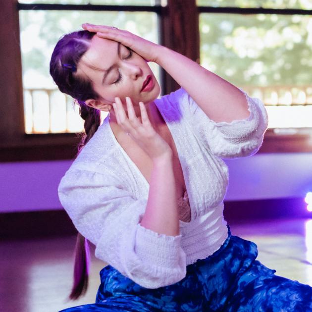 Dancer with long braid sitting on floor holding head to one side 