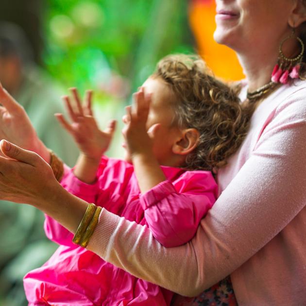 Adult and child in lap, wearing pink, clapping and using hand gestures