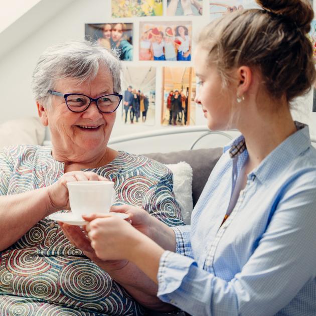 A young girl serving a cup of tea to a senior lady. 