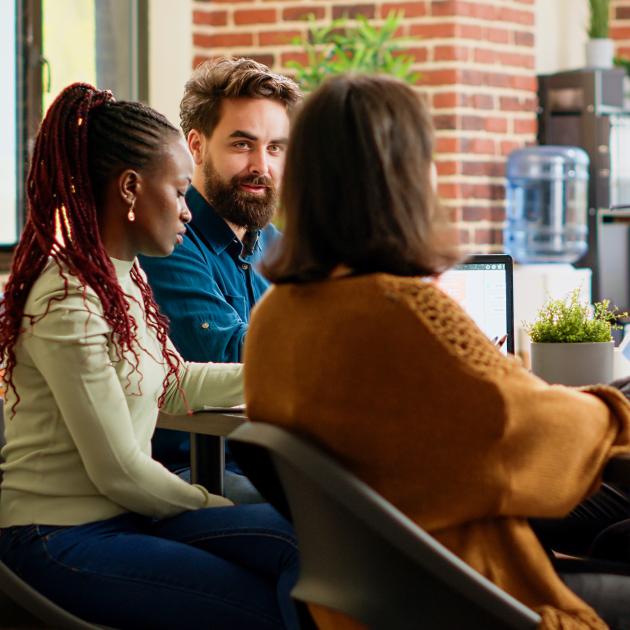 Three young professionals meeting around table with water cooler in background