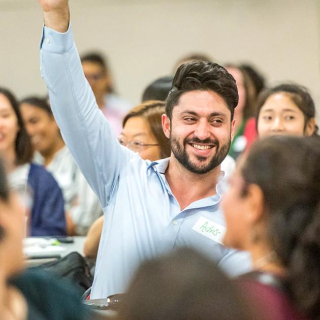 A photo of mail in a crowd smiling and raising one hand