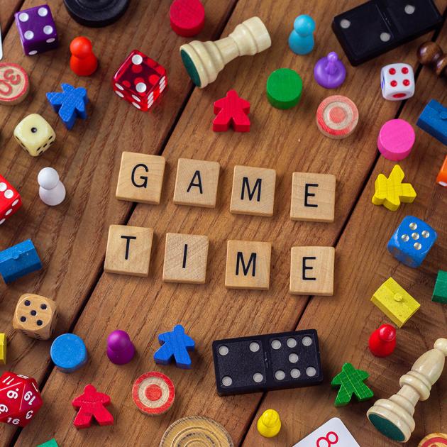 Chess and board game pieces scattered on a table with scrabble tiles spelling game time