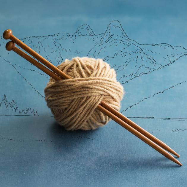 Ball of yarn with knitting needles through it, with north shore mountains in line art in the background