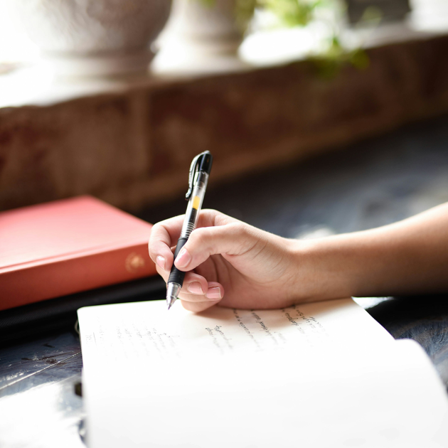 hand holds a pen - poised over a notebook, writing