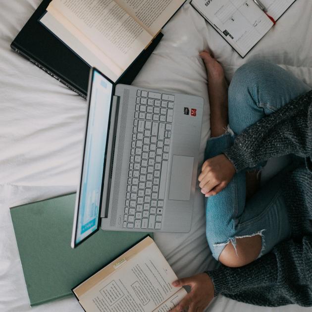 a person sitting cross legged on a bed with books and a laptop in front of them