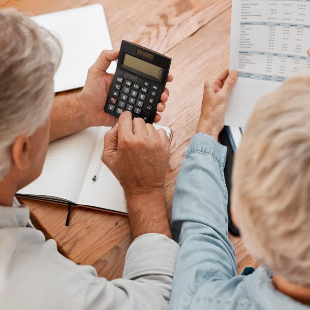 Two seniors looking at paperwork and holding calculator