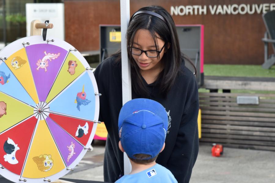 Teen helps young child with brightly coloured prize wheel at outdoor event