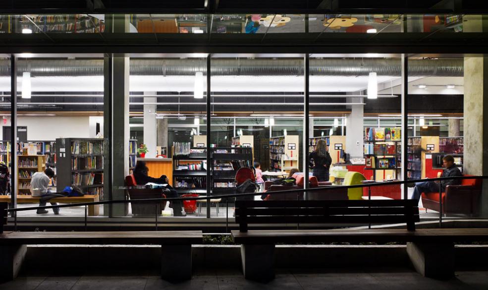 Photograph of the City Library building at night. There are people in the windows reading books and relaxing.