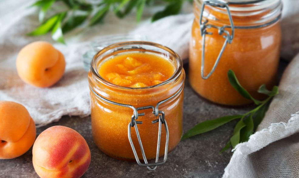 A photo of jars of peach jam with peaches in the background