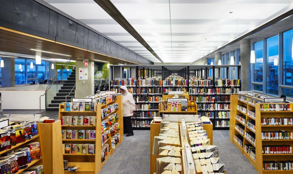 Picture of stacks of library books inside a library with one person wearing a white sweatshirt browsing