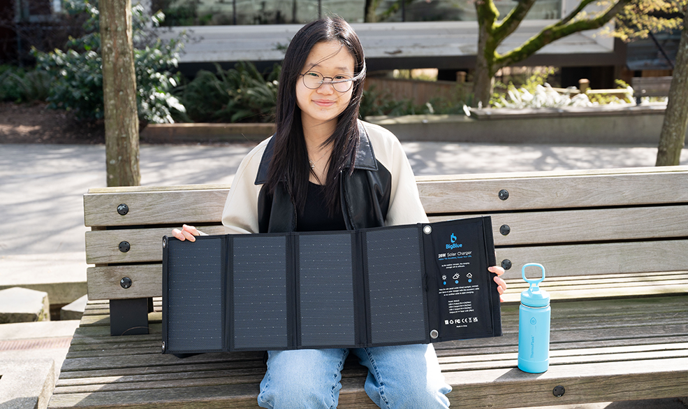 A young woman sitting on a bench holding a portable solar panel