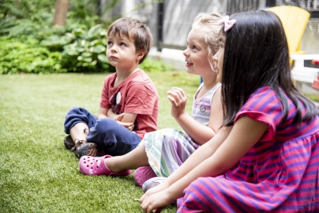 Three children sitting in a garden listening to a story