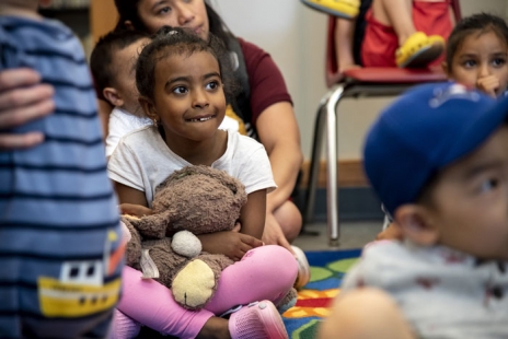 child sitting on the floor listening to a story holding a teddy bear
