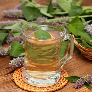 Glass mug with herbal tea in foreground, leaves and flowers behind